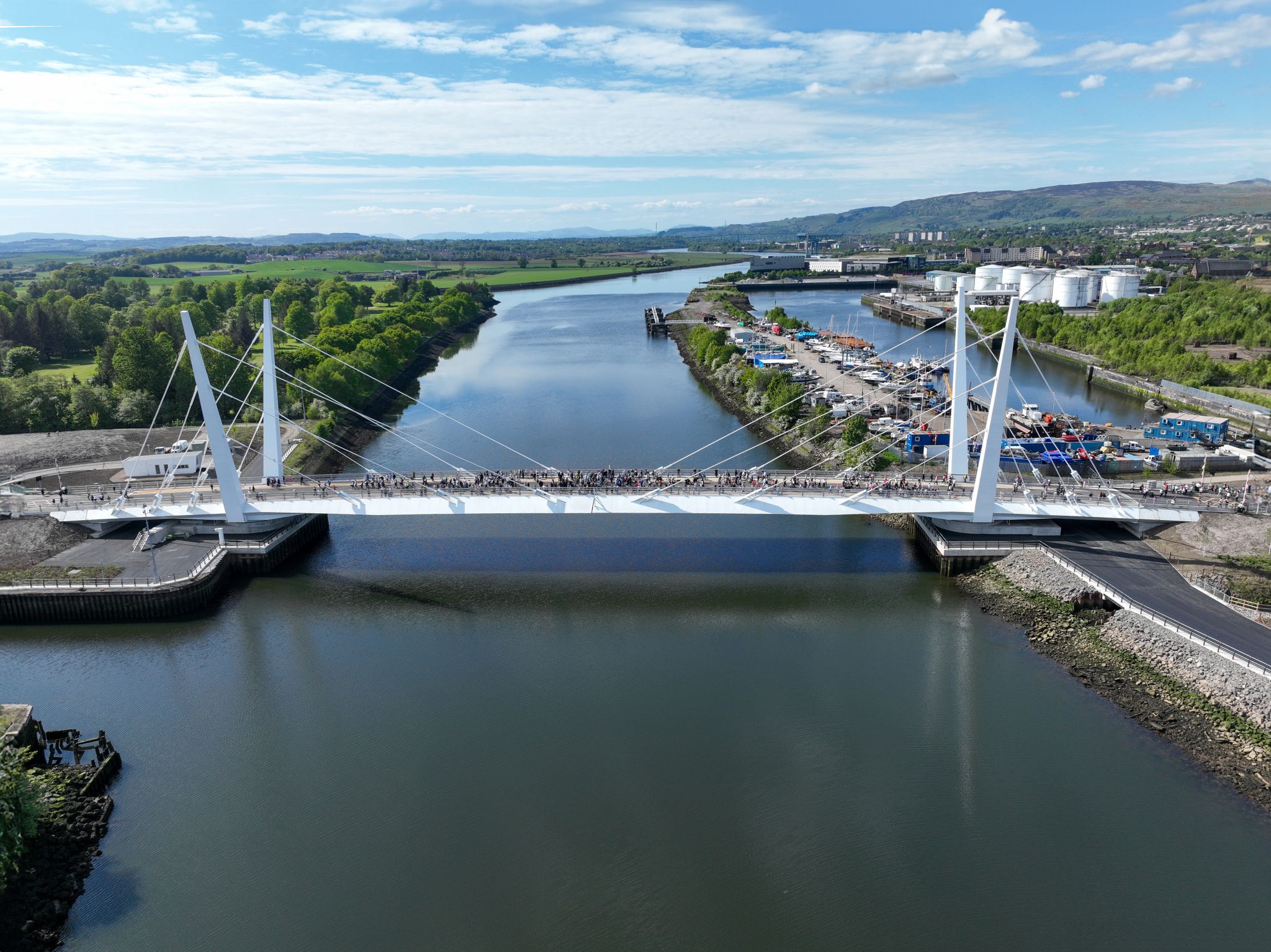 Aerial view of Renfrew Bridge spanning the River Clyde, with people crossing the bridge and industrial facilities and green landscape in the background.