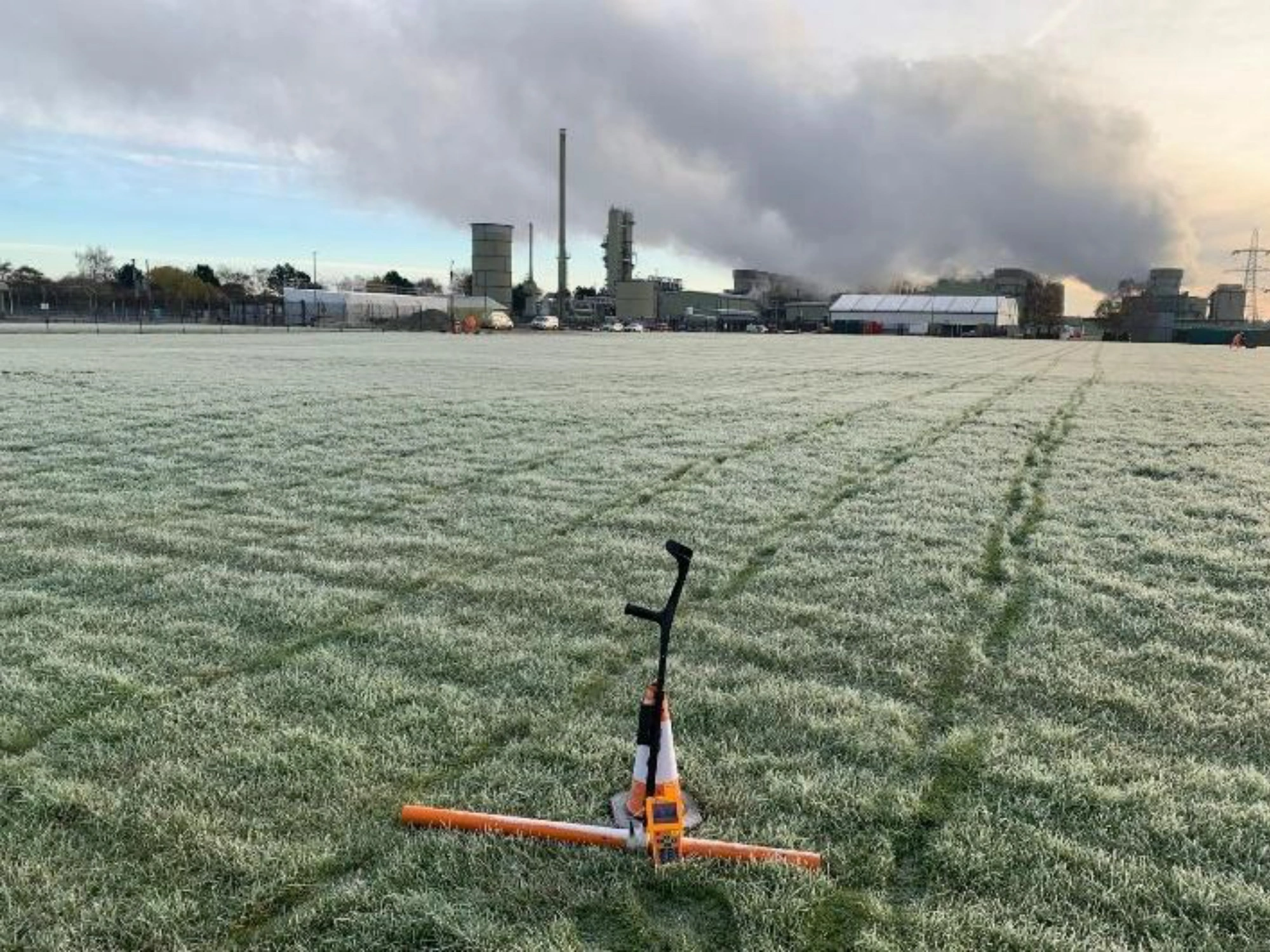 A large expanse of frosty grass with a peice of land surveying equipment positioned on it and Uniper Energy buildings in the background.