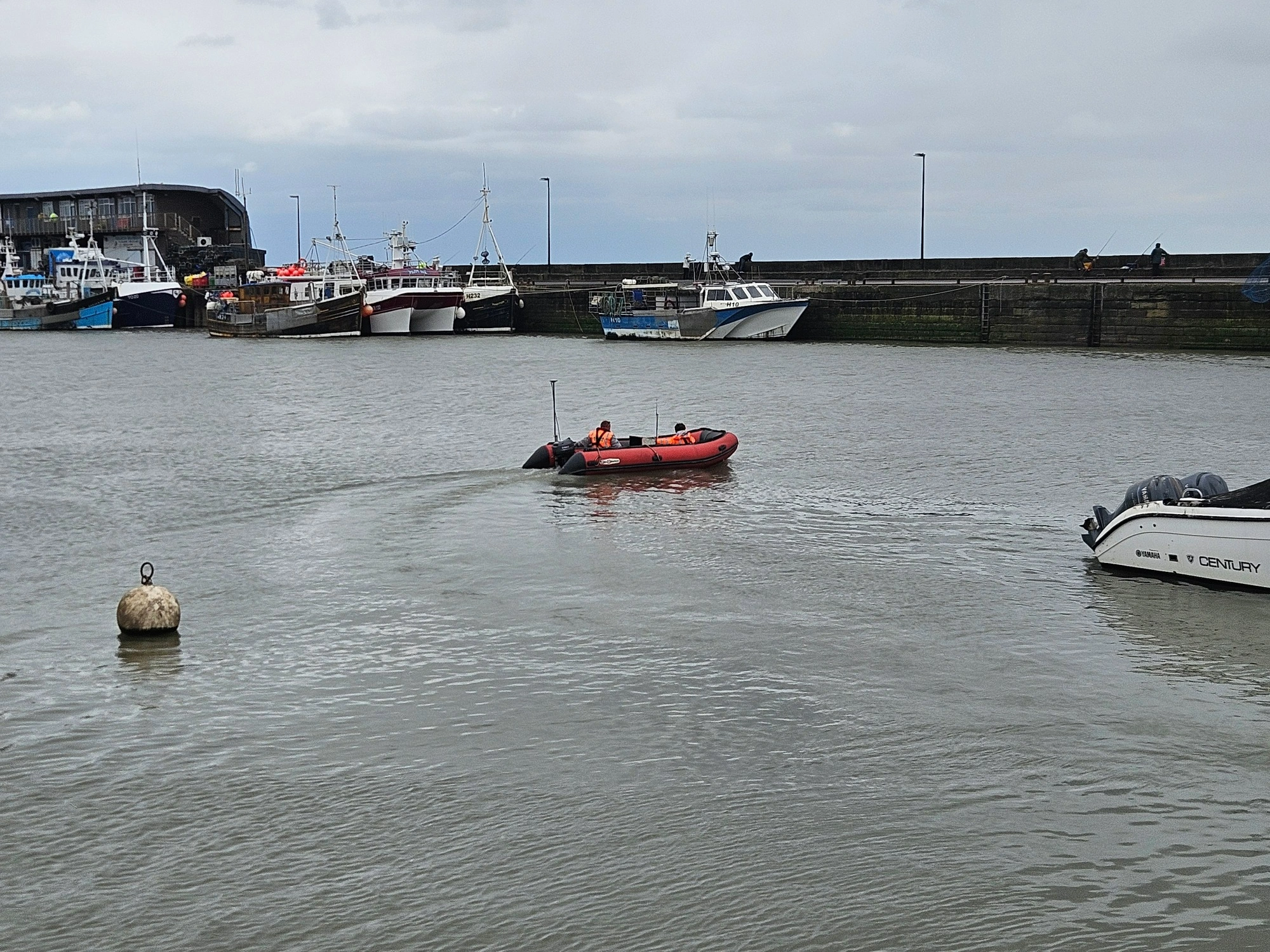 MHLS-bridlington-harbour-case-study (1)-6 MHLS land surveyors steering an orange boat around Bridlington Harbour on a cloudy day.